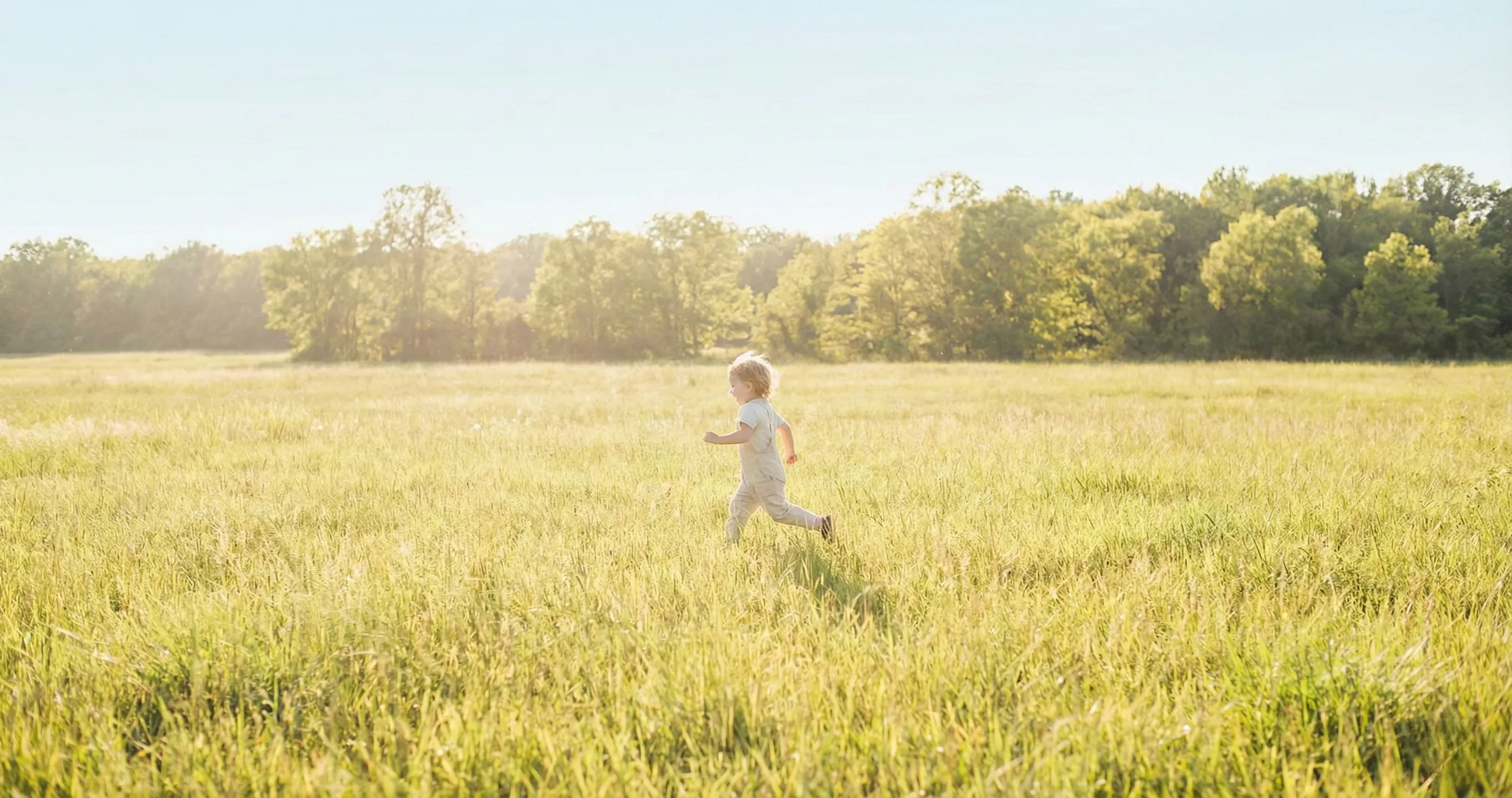 Child running through a sunlit meadow toward a treeline - green time for kids
